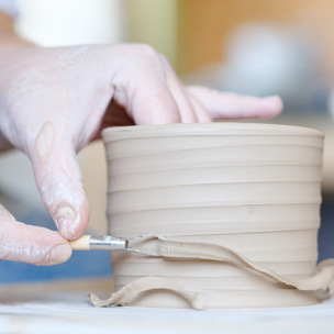 someone scrapes clay away on pot using tool
