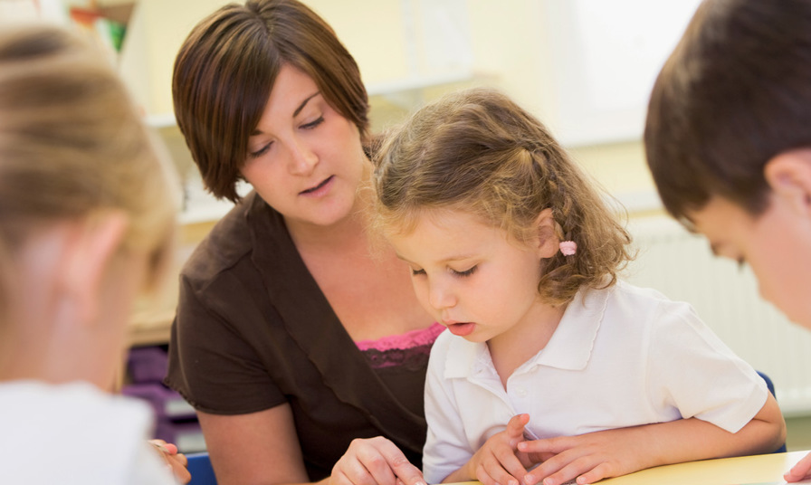 teaching assistant sat with school child looking at book
