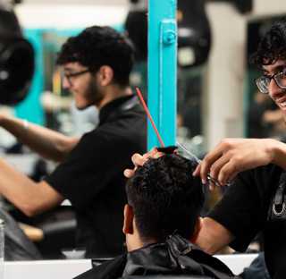 smiling barbering student cuts clients hair