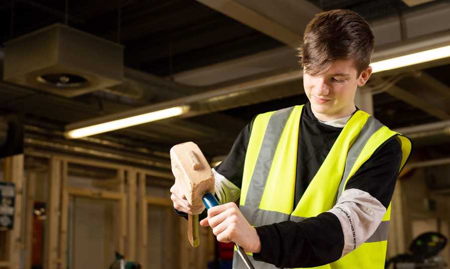 young man in hi-vis vest using chisel and mallet in joinery workshop