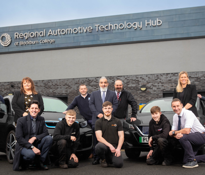 group of people stood or crouched in front of cars in front of Regional Automotive Technology Hub at Blackburn College