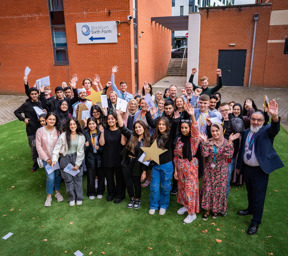 group of students and staff celebrating with arms in the air and holding gold stars