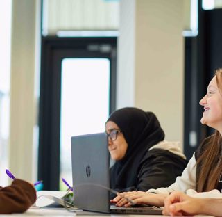 group of students working around table with laptop smiling