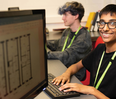 student smiling to camera working at computer with architectural drawings
