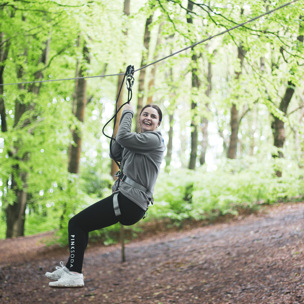 young woman smiles as she zooms down zip wire whilst attached in seat
