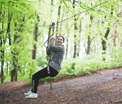 young woman smiles as she zooms down zip wire whilst attached in seat