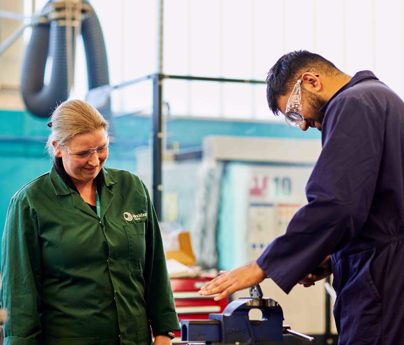 tutor looks on as engineering student uses machinery in engineering workshop