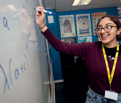 female student writes equation on white board