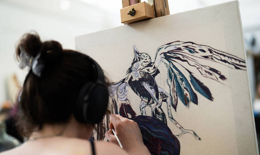 A girl painting a picture of a bird on to a canvas
