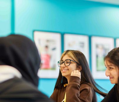 Student with glasses on smiling alongside two other students in class.