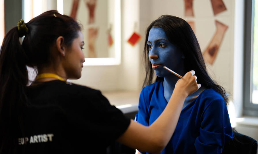 Student applying blue makeup to a fellow student 