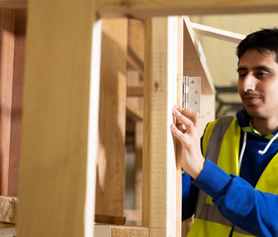 student in hi-vis vest aligning hinge on timber frame