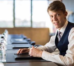 young man smartly dressed sits at boardroom table