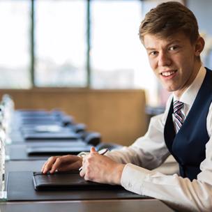 young man smartly dressed sits at boardroom table