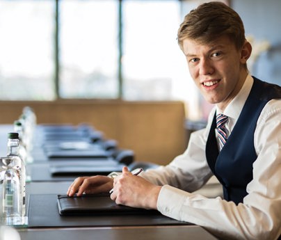 young man smartly dressed sits at boardroom table