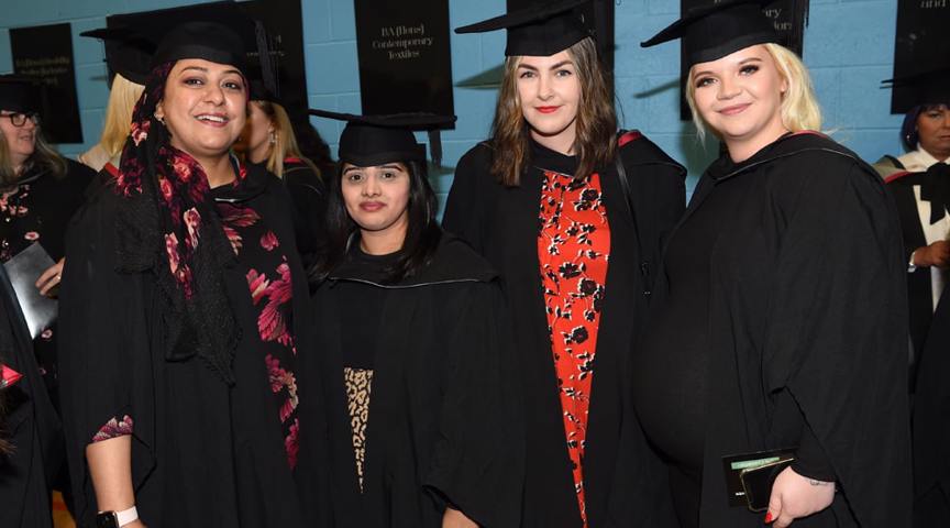 group of women in graduation cap and gowns smiling to camera