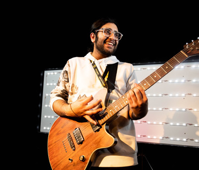 student playing electric guitar with lights in background