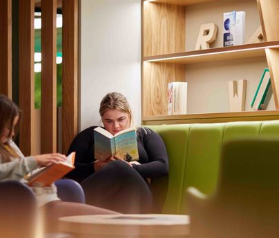 2 students sat in the Exchange learning zone reading books. Some bookshelves are beside them