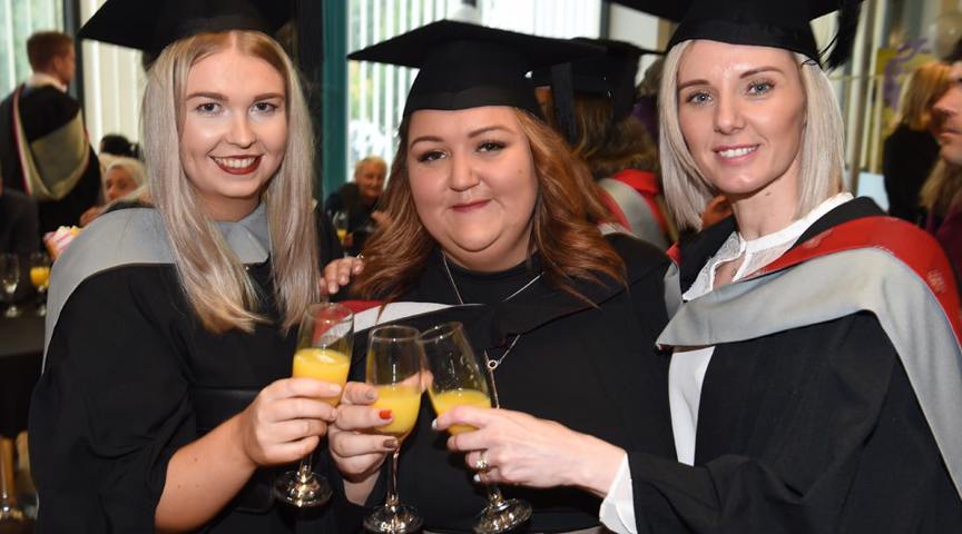 3 women in graduation cap and gowns holding glasses of orange juice