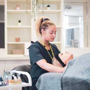 student beauty therapist with client laid down on table with tray of beauty products beside