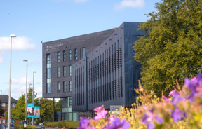 Beacon Centre building on campus at Blackburn College in sunshine. Purple flowers in foreground.