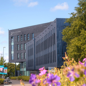 Beacon Centre building on campus at Blackburn College in sunshine. Purple flowers in foreground.