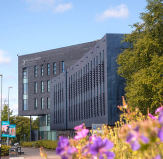Beacon Centre building on campus at Blackburn College in sunshine. Purple flowers in foreground.