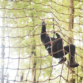 person hangs to climbing rope wall in forest
