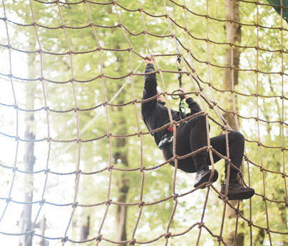 person hangs to climbing rope wall in forest