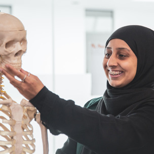 female student wearing headscarf smiling and holding model skeleton