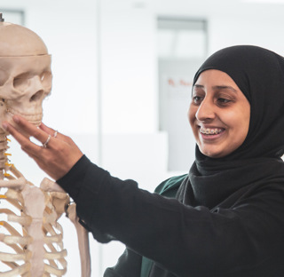female student wearing headscarf smiling and holding model skeleton