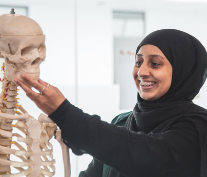 female student wearing headscarf smiling and holding model skeleton