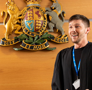 man in black robes smiling stood next to crest on wall