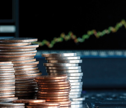 close up of piles of coins with financial stocks on screen in background