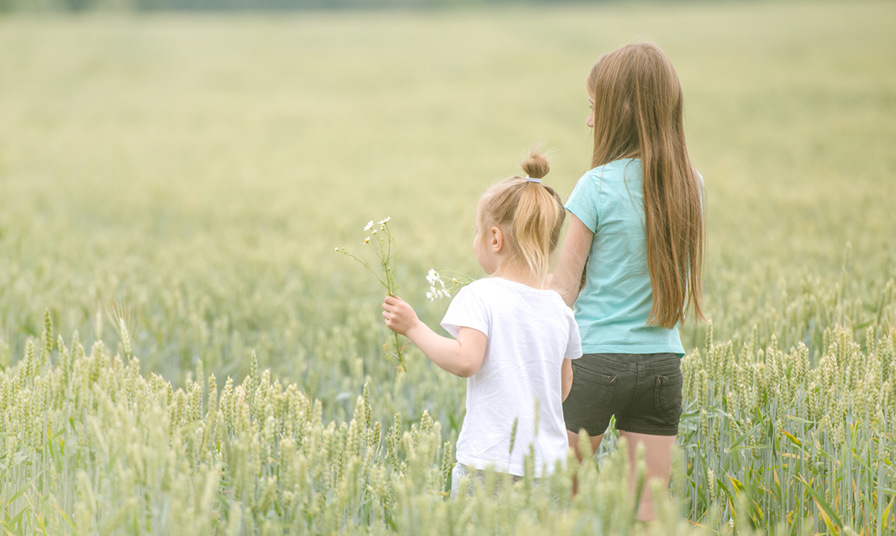 2 young children walking through filed holding flowers
