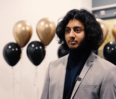 young man in suit stands in front of black and gold balloons