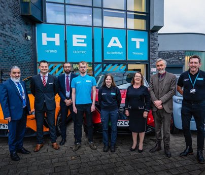 group of people stood in front of cards and HEAT Hybrid Electric Automotive Training building