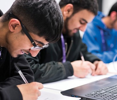 students writing next to open laptop