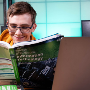 student reading Information Technology book behind open laptop