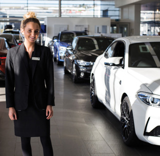 smartly dressed young woman stands in car showroom