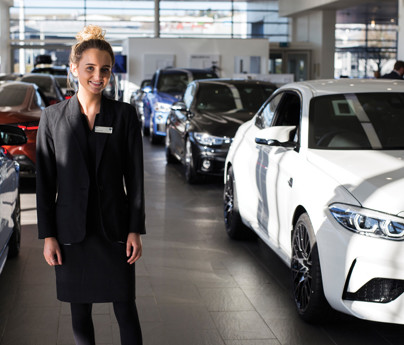 smartly dressed young woman stands in car showroom