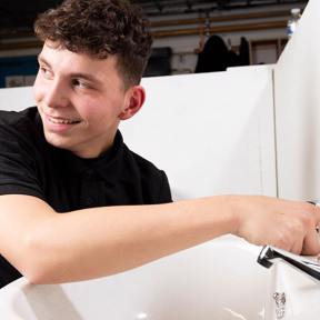 plumbing student smiles whilst working at sink