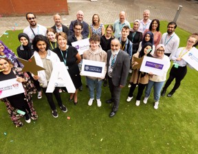 group of staff and students celebrating holding stars and large As and boards saying Lancaster University, Durham University, University of Oxford, Manchester University and University of Central Lancashire