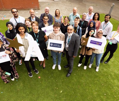 group of staff and students celebrating holding stars and large As and boards saying Lancaster University, Durham University, University of Oxford, Manchester University and University of Central Lancashire