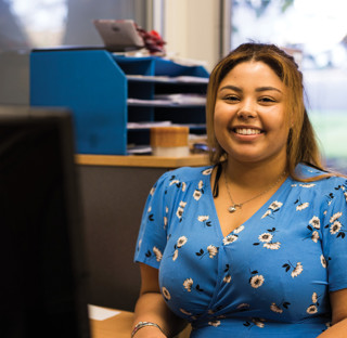 woman smiling to camera sat at office desk