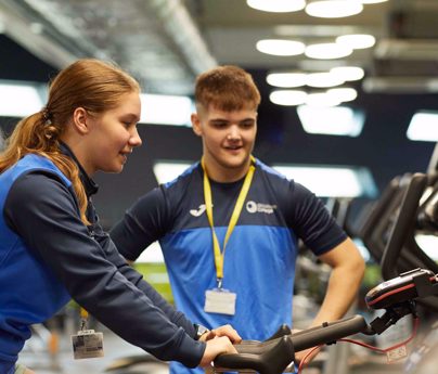 sports student watches over another student using gym bike equipment
