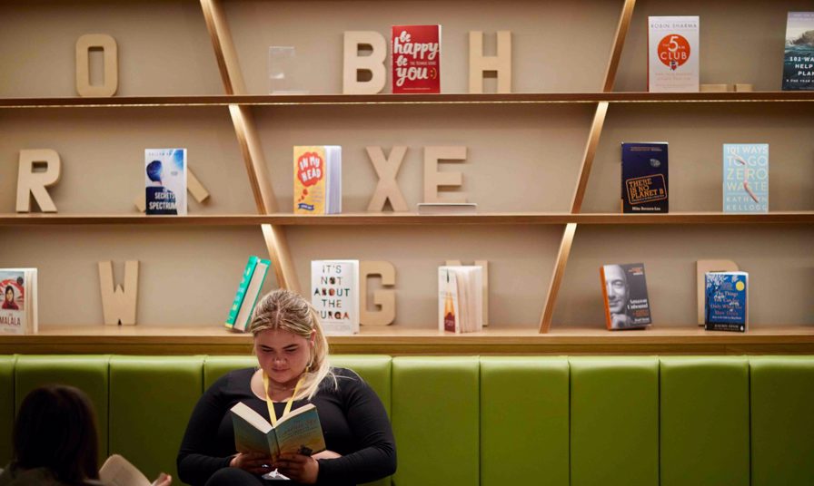 students sat in the Exchange learning zone reading a book. A bookshelf is behind her
