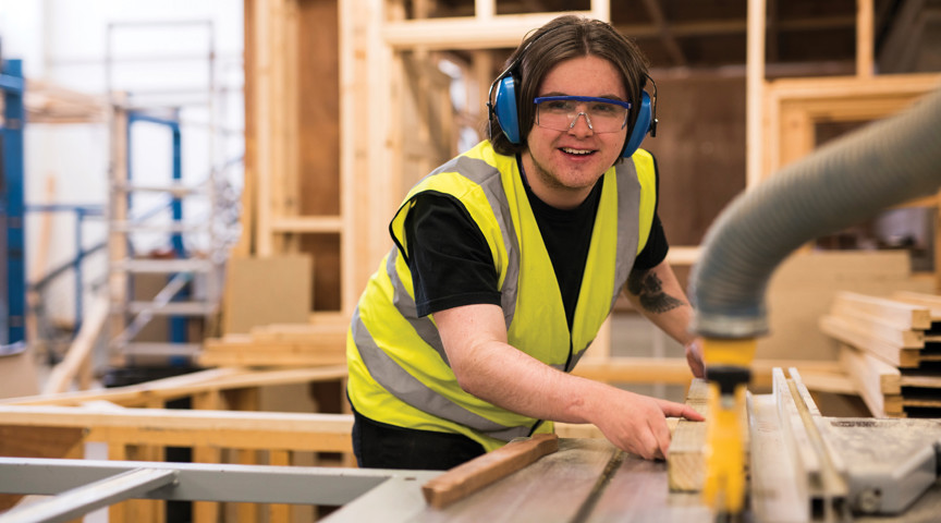 man wearing protective goggles and headphones operates joinery equipment