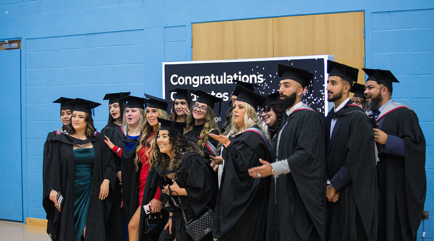 Group of graduates posing for phot in front of stand saying Congratulations