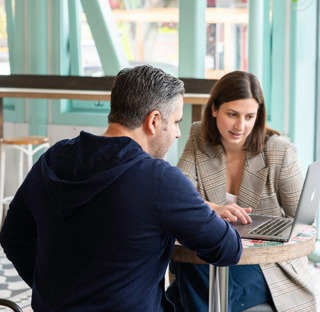 1 man and 1 woman talking looking at laptop on table